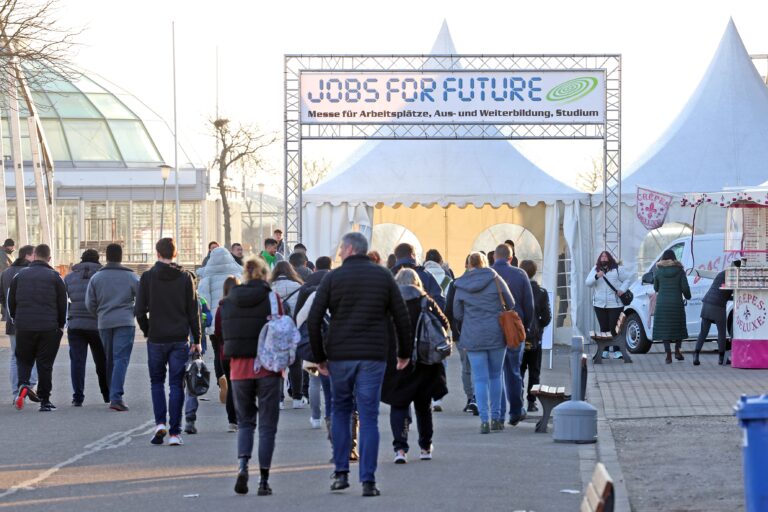 Mehrere Menschen auf dem Weg auf einem Messegelände mit dem Eingangschild: Jobs for future