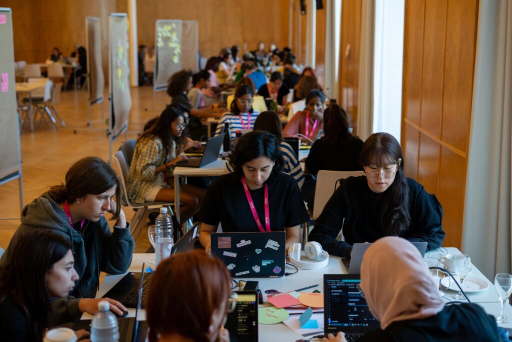 Mehrere Menschen sind in Gruppen an Tischen mit Laptops vor ihnen aufgestellt.